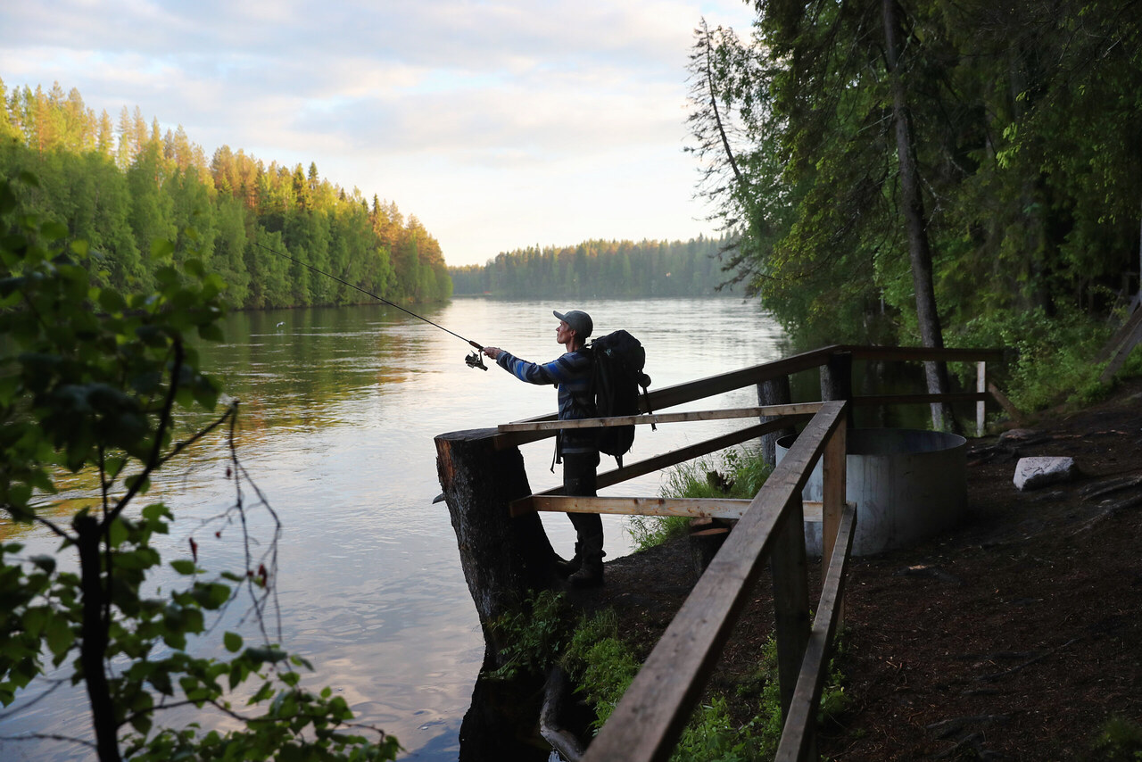 Kalastaja veneessä tyynellä Oulujärvellä auringonlaskun aikaan, hiljaisessa ja luonnonkauniissa maisemassa.