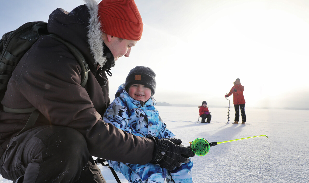 Perhe nauttii pilkkimisestä rauhallisella Oulujärven jäällä – täydellinen talviaktiviteetti luonnon keskellä.